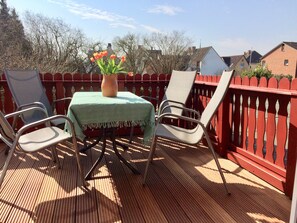 Eine Holzterrasse mit Tisch und Stühlen, einer Blumenvase und einem roten Zaun.