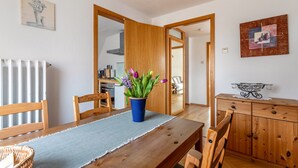 A dining area with a wooden table, chairs, a blue vase with flowers, a radiator, and a wooden cabinet.