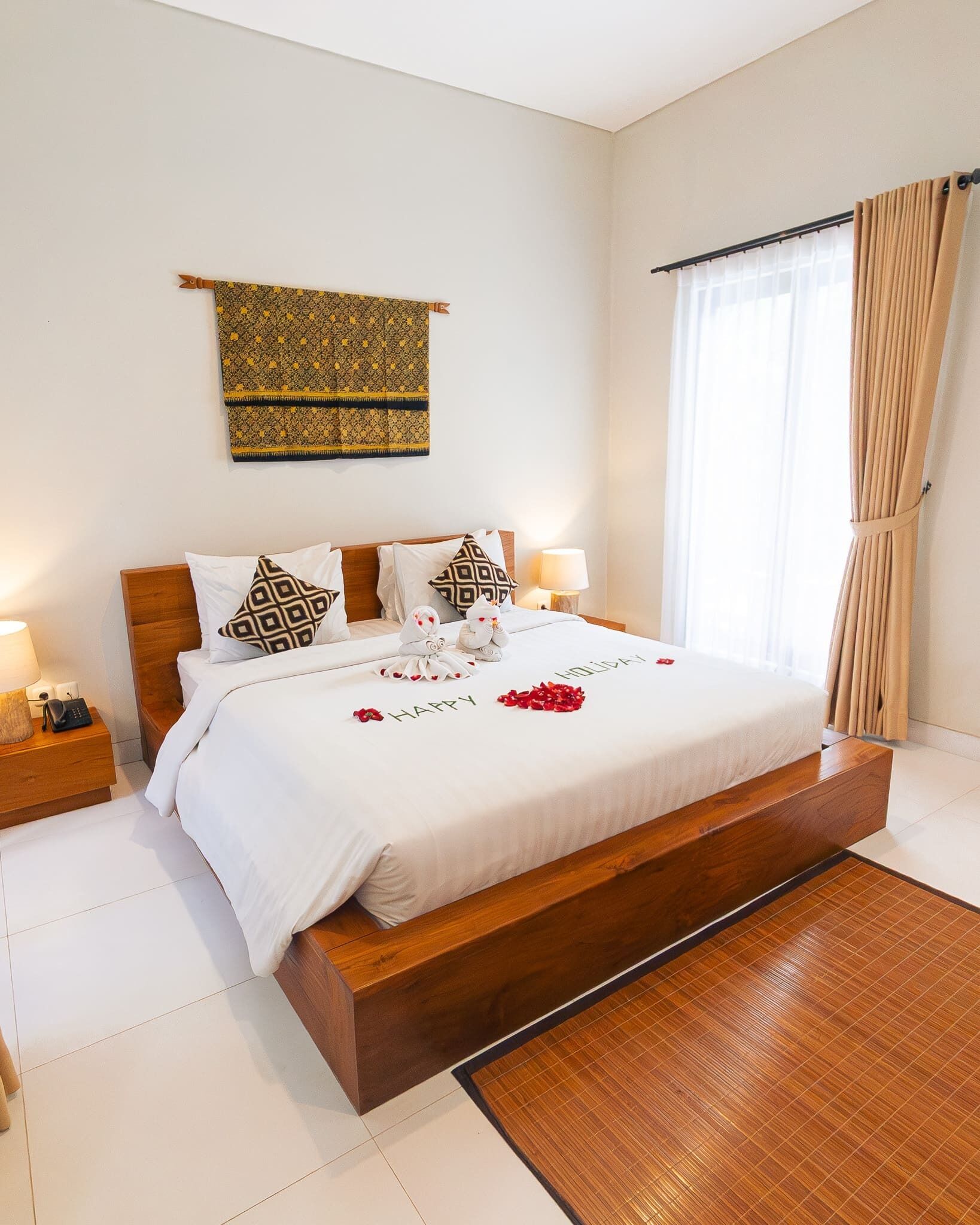 Una cama bien hecha con una colcha blanca, dos lámparas de noche y un cojín decorativo.