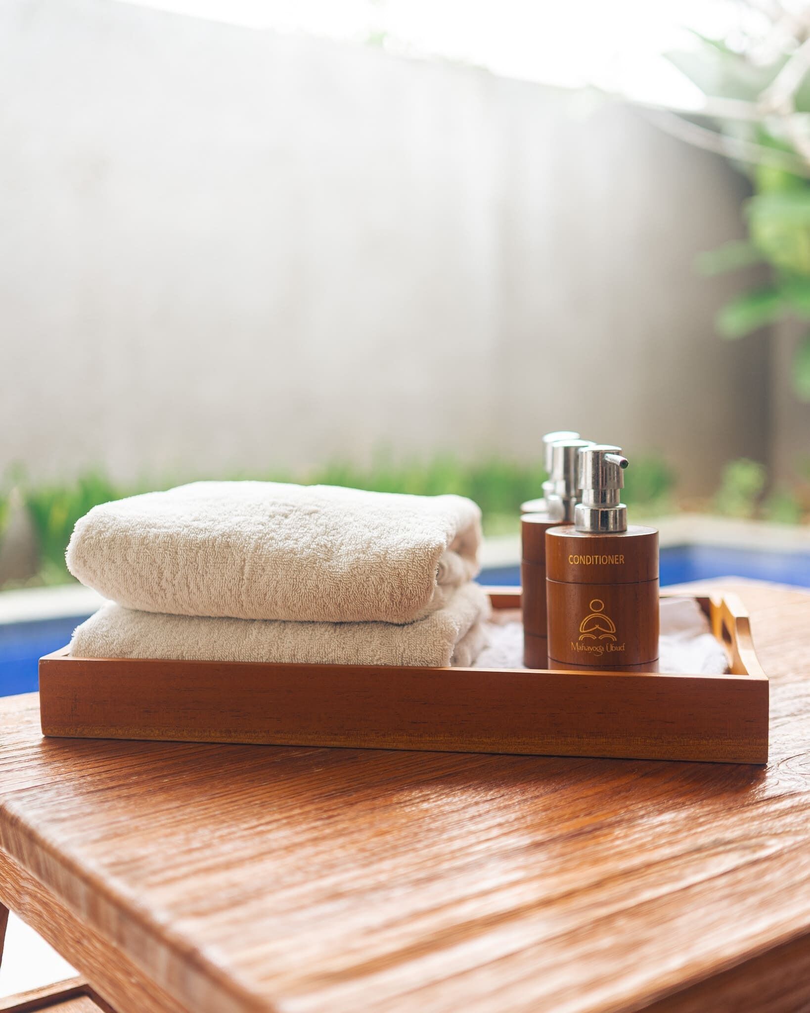 A wooden tray with a folded towel and a brown bottle labeled "Conditioner" on a wooden table.