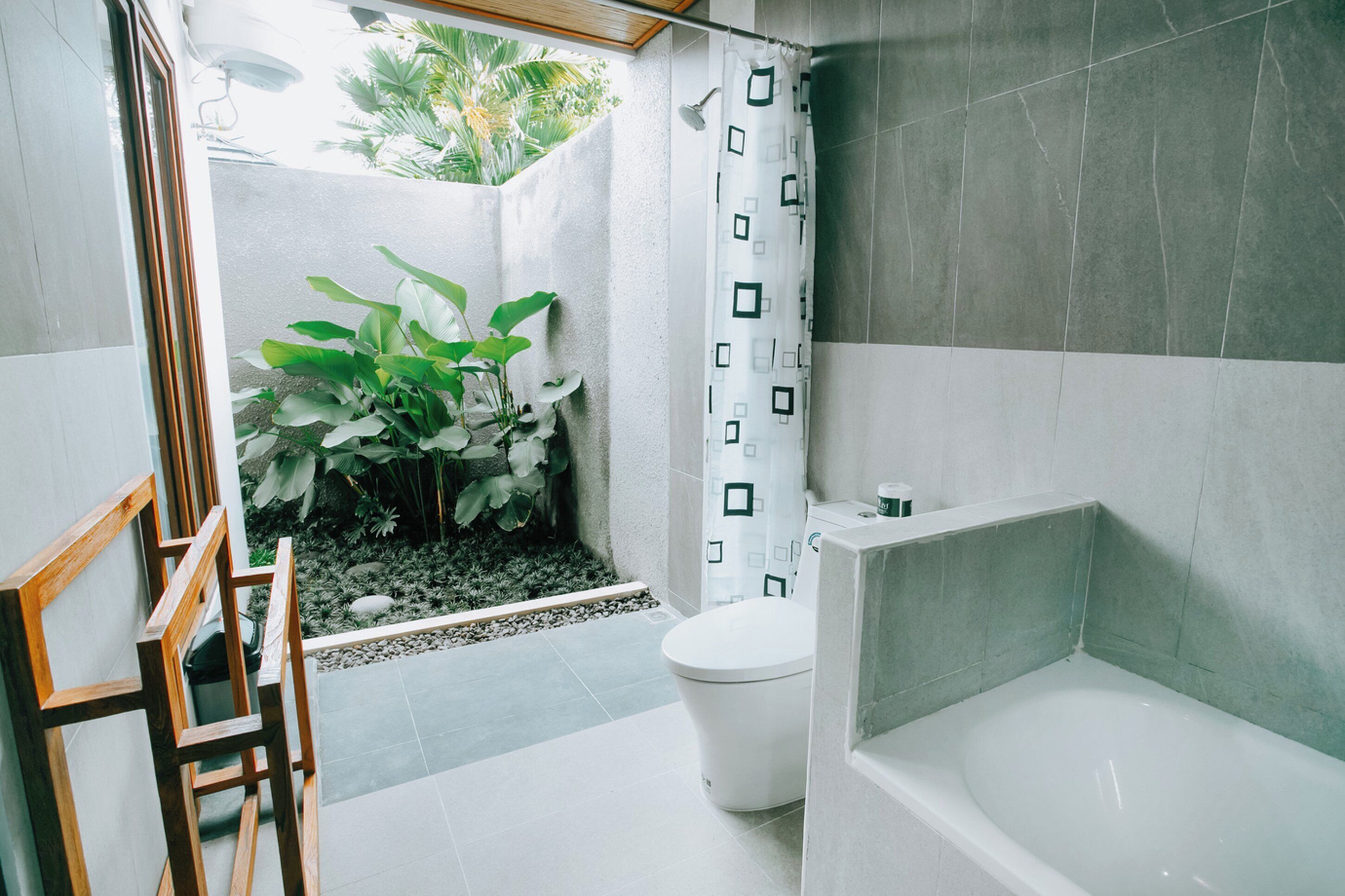A bathroom with a bathtub, toilet, shower curtain, and a small garden area with plants.
