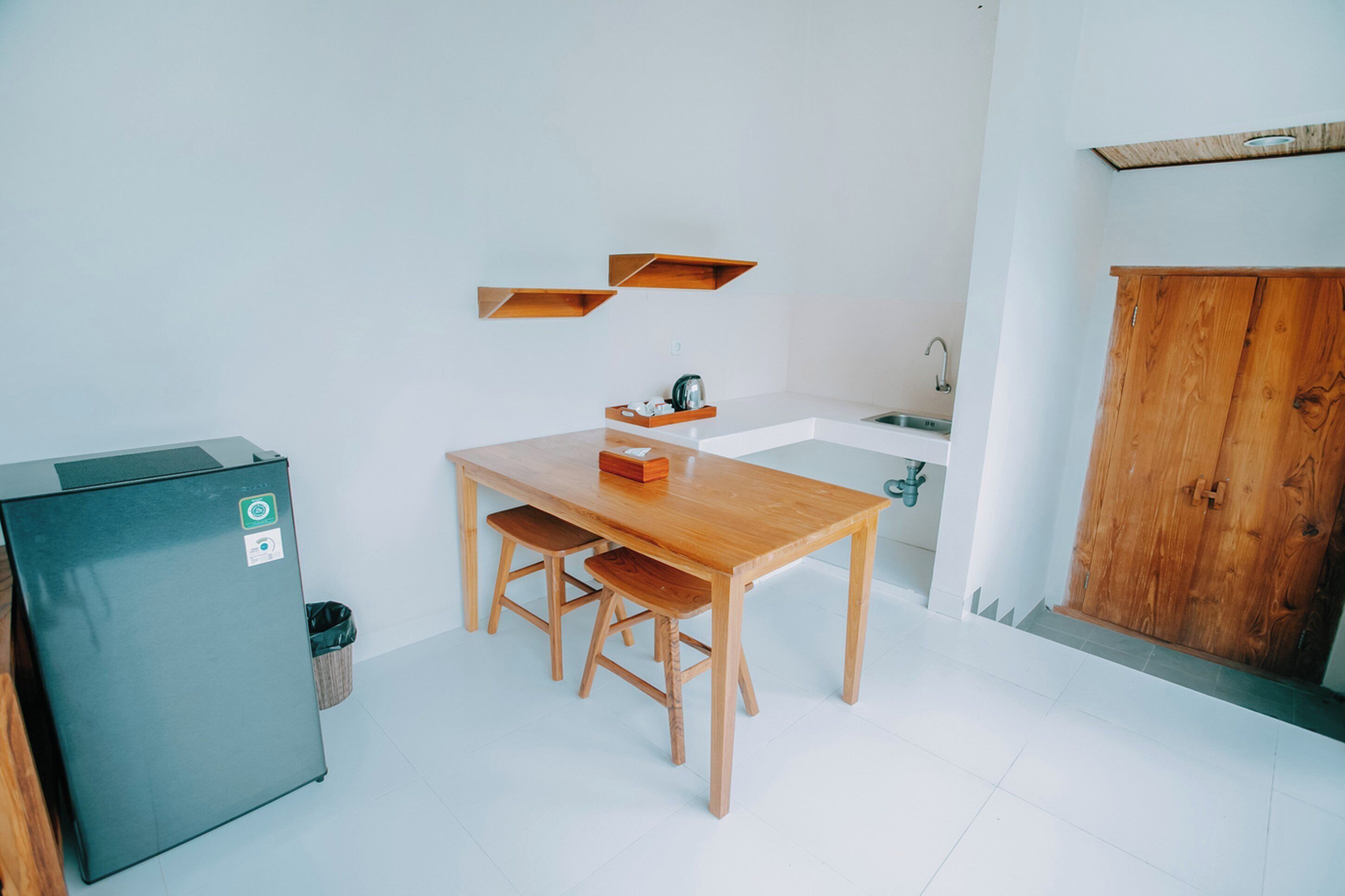 A compact kitchen with a wooden table and chairs, a black refrigerator, and a wooden cabinet.