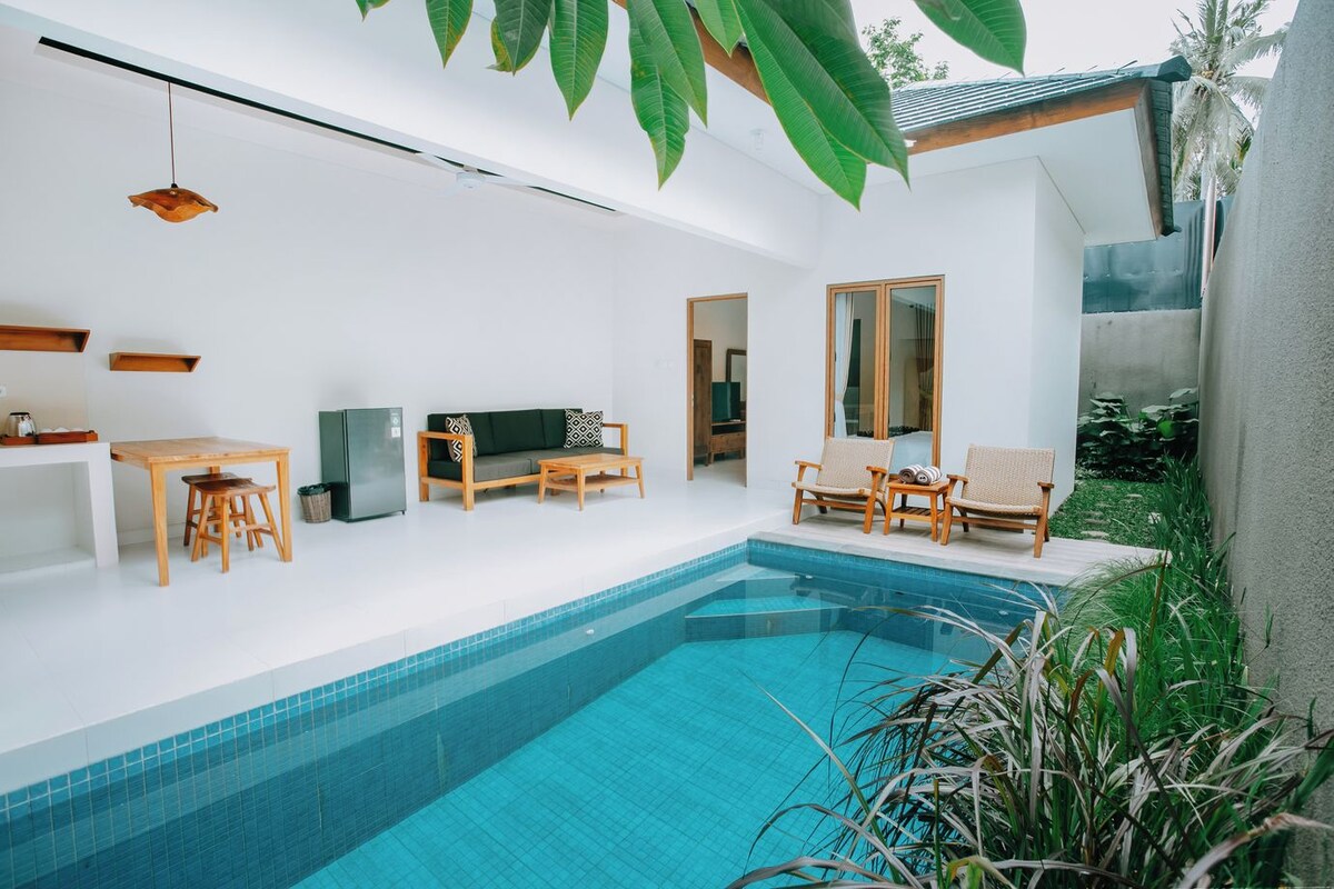 A modern indoor swimming pool with a clear blue water, wooden furniture, and a minimalist design.
