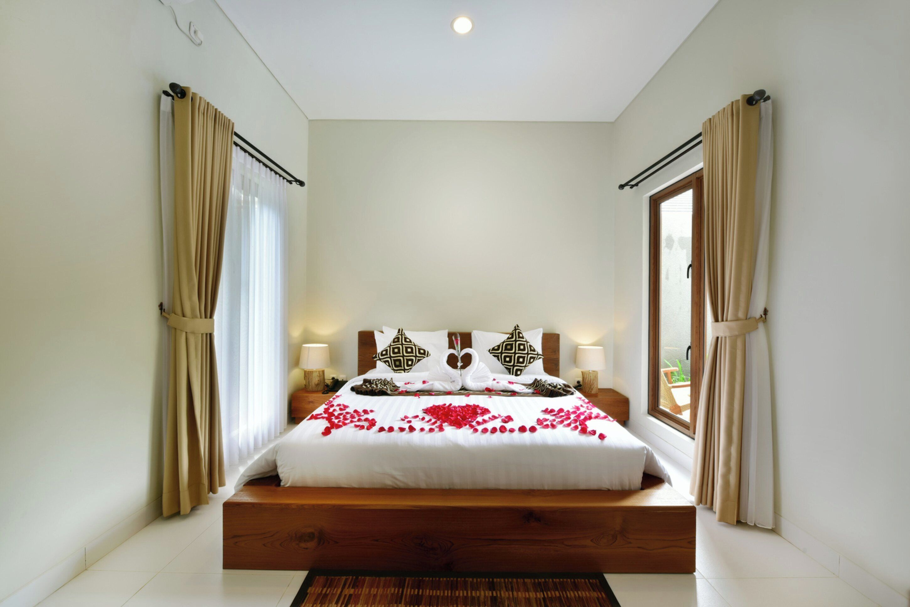 A bedroom with a wooden bed, white bedding, and a window with curtains.