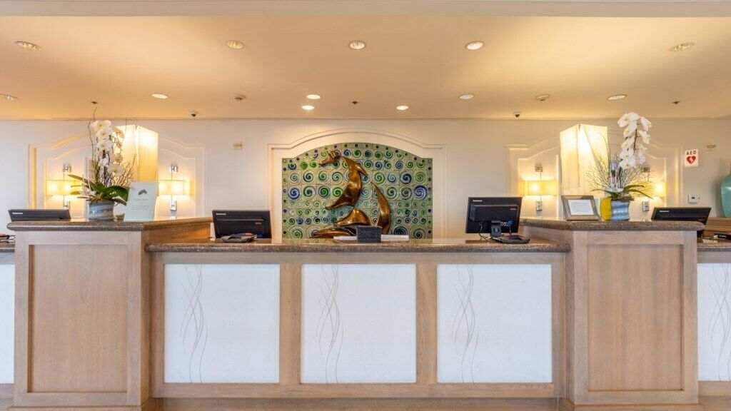 A reception desk with a decorative sculpture, two computer monitors, and a patterned wall behind.