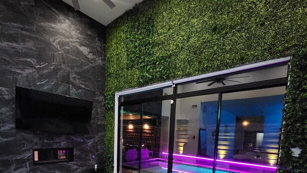 Een moderne woonkamer met een groene wand, een flatscreen televisie, uitzicht op een zwembad en een plafondventilator.