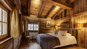 Un dormitorio de cabaña de madera con una cama, una silla, una ventana y un cuadro en la pared.
