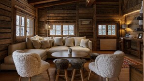 Interior acogedor de una cabaña de troncos con un sofá grande, sillones mullidos, una mesita redonda y una chimenea.