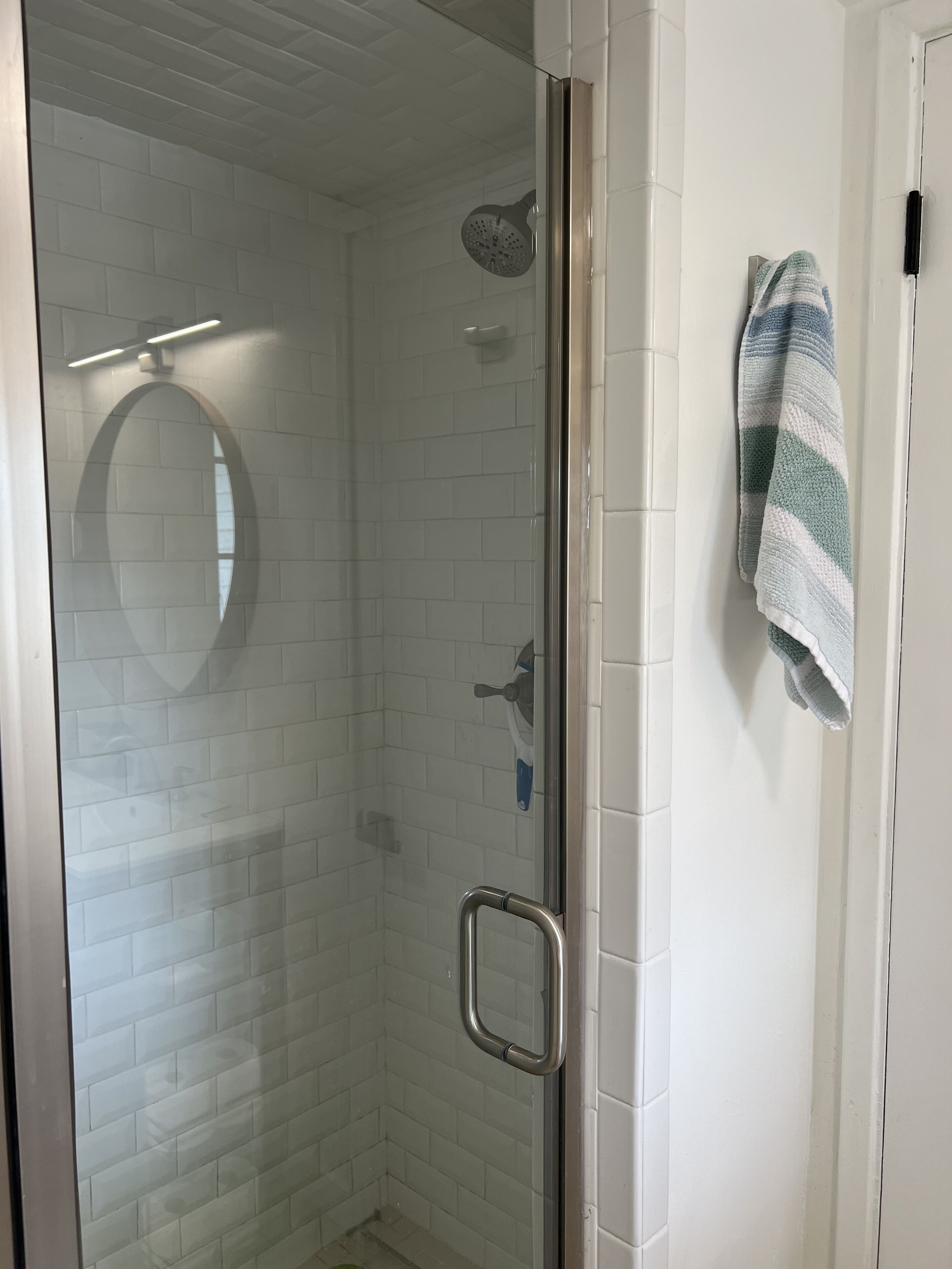 A glass-enclosed shower with a handheld showerhead and a handheld faucet.