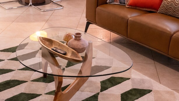 Un salon moderne avec une table basse en verre, un canapé en cuir et un tapis à motifs.