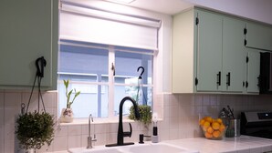 Une cuisine équipée d’un  évier à deux bacs, d’une fenêtre avec des stores et d’une plante en pot posée sur le plan de travail.