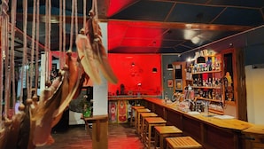 Zona de bar con taburetes de madera, mostrador y estantes con botellas.
