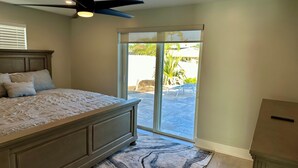 A bedroom with a bed, a ceiling fan, a sliding glass door leading to a patio, and a small cabinet. - Sea U Soon - Luxury Dock Home (Fort Myers Beach)