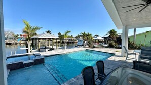 A swimming pool with a dock and lounge area, surrounded by palm trees and a clear sky. - Sea U Soon - Luxury Dock Home (Fort Myers Beach)