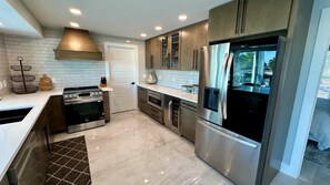 A modern kitchen with stainless steel appliances, a brick backsplash, and a large window. - Sea U Soon - Luxury Dock Home (Fort Myers Beach)