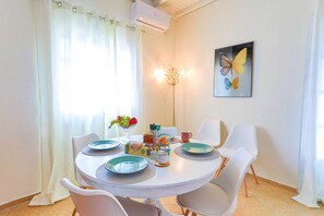 A dining area with a round table, white chairs, and a painting of butterflies on the wall. - Villa Serenita in Agios Georgios (Corfu)