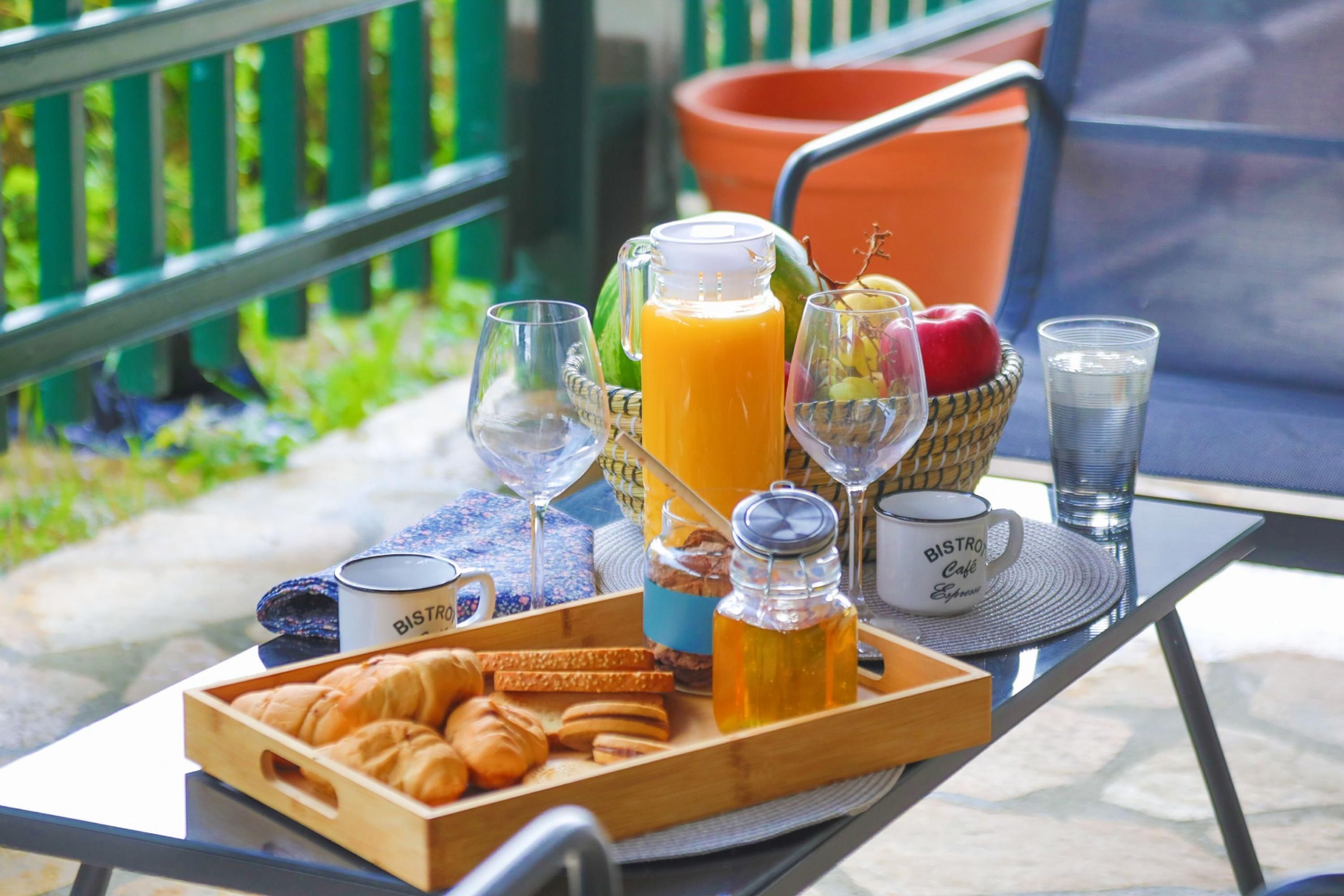 Een ontbijtkar met croissantjes, sap en een fles honing op een tafel buiten.