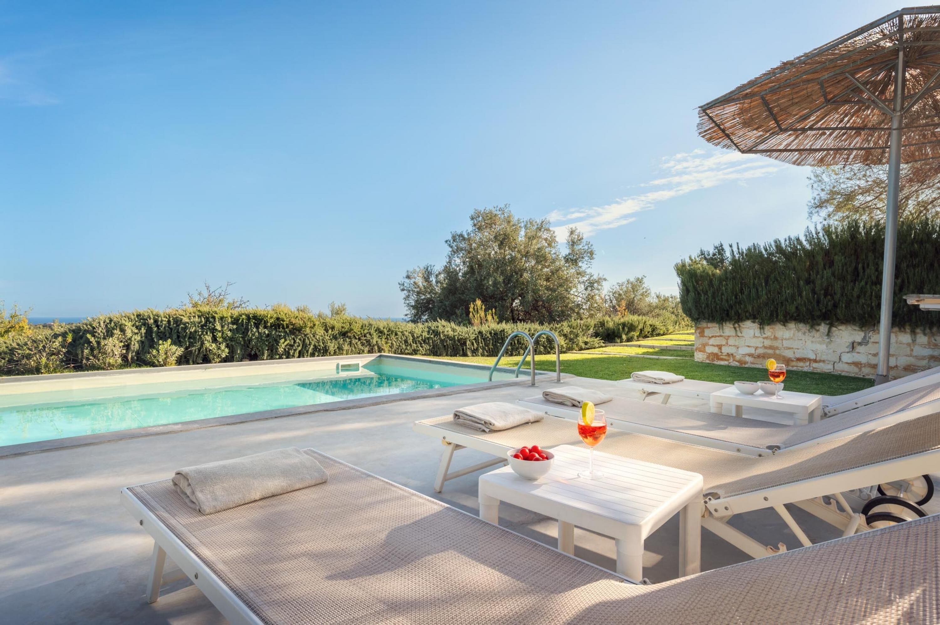 A poolside area with lounge chairs, a table with a drink, and a view of the sea.