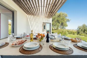 An outdoor dining table set with plates, cutlery, and bottles, surrounded by a pergola and a scenic view. - Villa Il Cavaliere Dependance by Elite Villas (Noto)