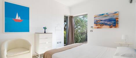 Une chambre moderne avec un grand lit, une chaise, une commode et deux tableaux.