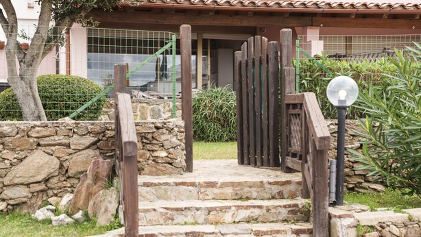 A stone staircase leading to a wooden door with a glass panel, surrounded by greenery and a stone wall. - Verde Mare in Punta Pedrosa (Golfo Aranci)