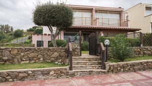 A stone-walled entrance with a wooden staircase leading to a house with a tiled roof and a balcony. - Verde Mare in Punta Pedrosa (Golfo Aranci)