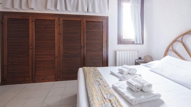 Ein Schlafzimmer mit großem Holzschrank, einem Bett mit weißer Bettwäsche und einem Fenster mit Vorhängen.