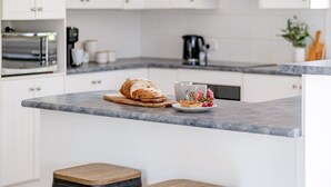 Une cuisine avec un plan de travail en marbre, une miche de pain, une assiette avec une pâtisserie et une machine à café.