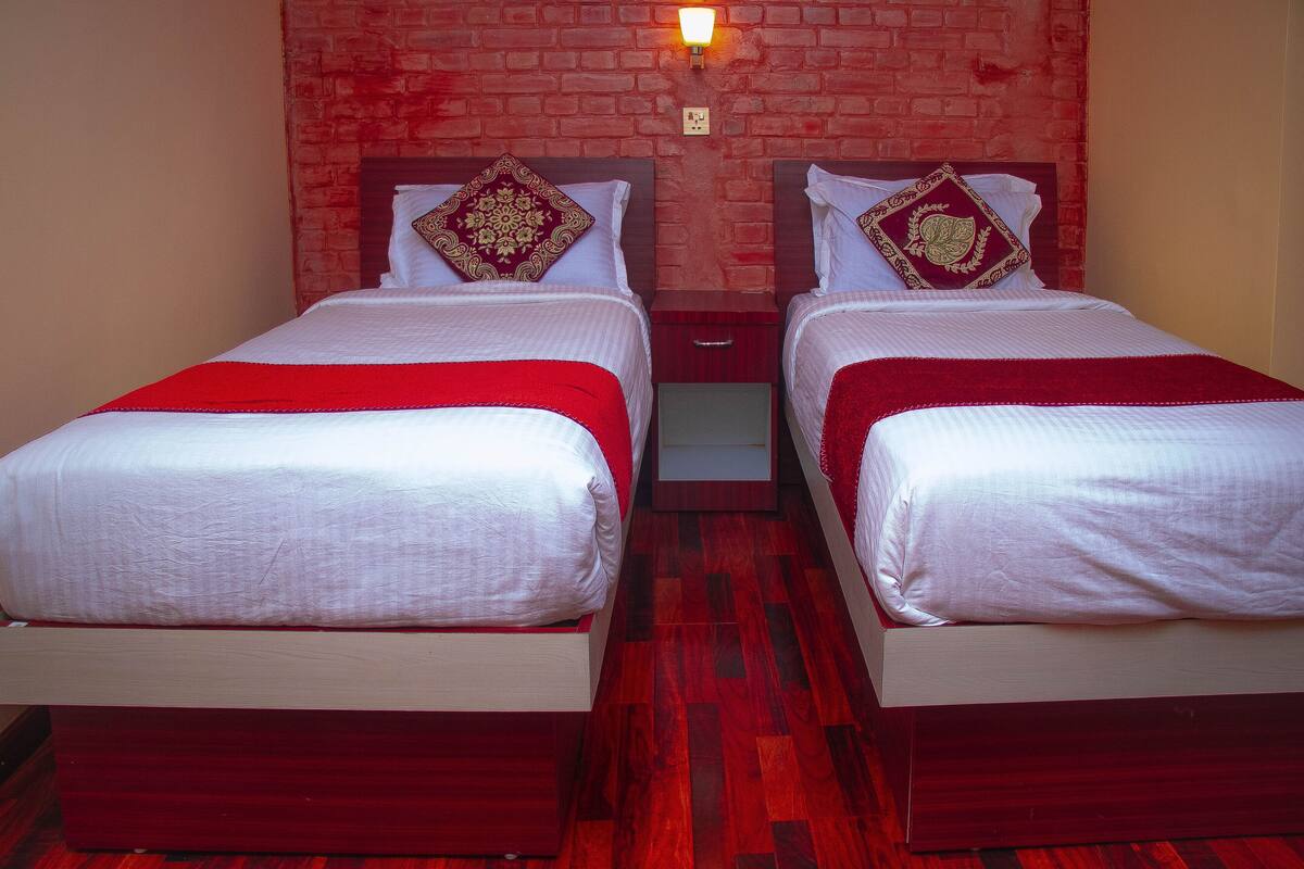 A room with two beds, each with a red bedspread and matching pillows, against a brick wall with a wall-mounted light.