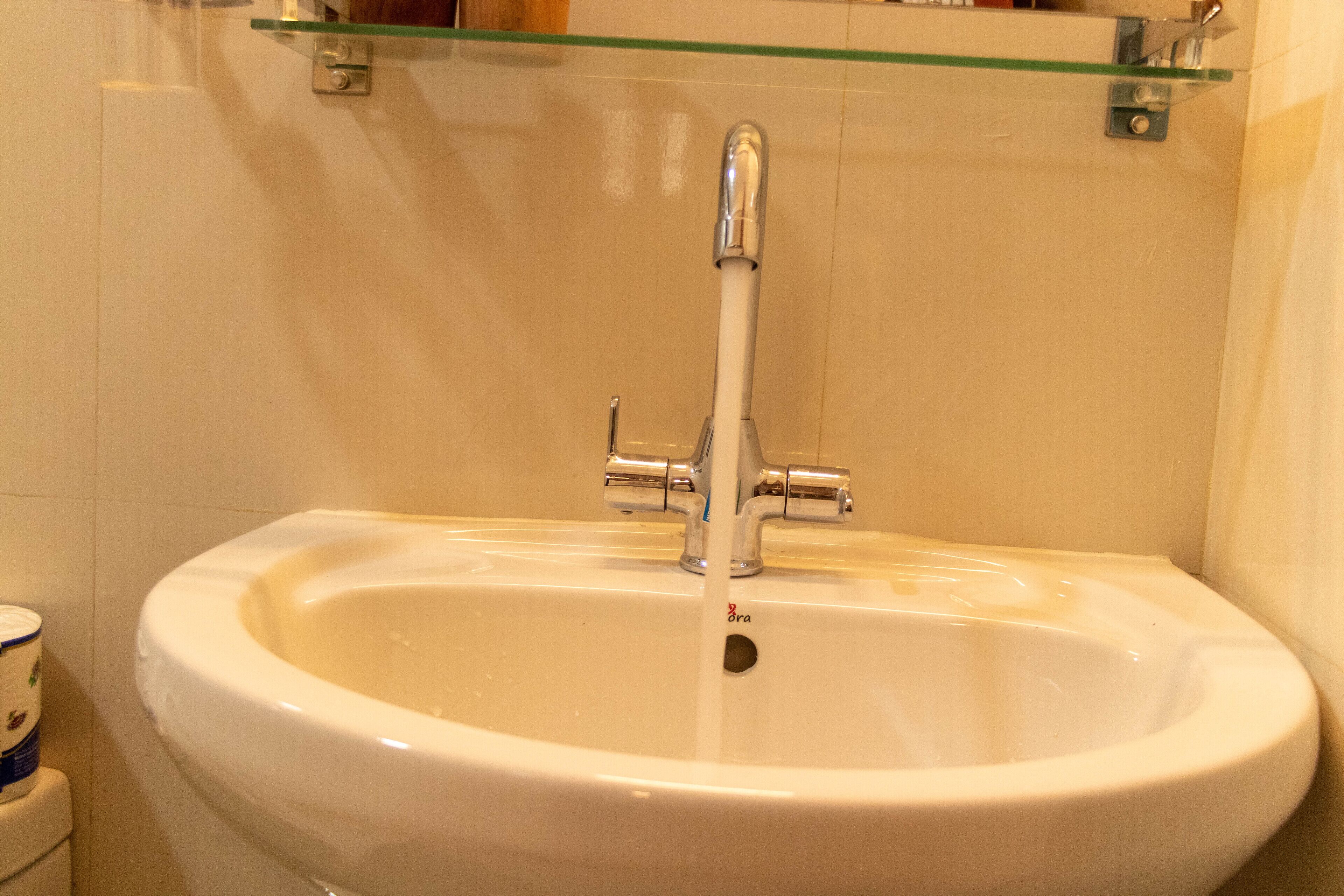Ein weißes Waschbecken mit Chromarmatur, eine Glasablage darüber und eine Toilette zur Linken.