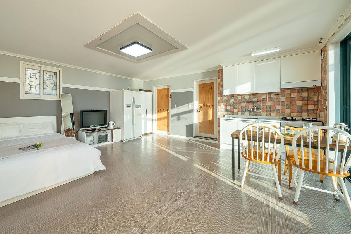 A hotel room with a bed, a TV, a kitchenette, and a dining area with chairs.