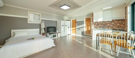 A hotel room with a bed, a TV, a kitchenette, and a dining area with chairs.