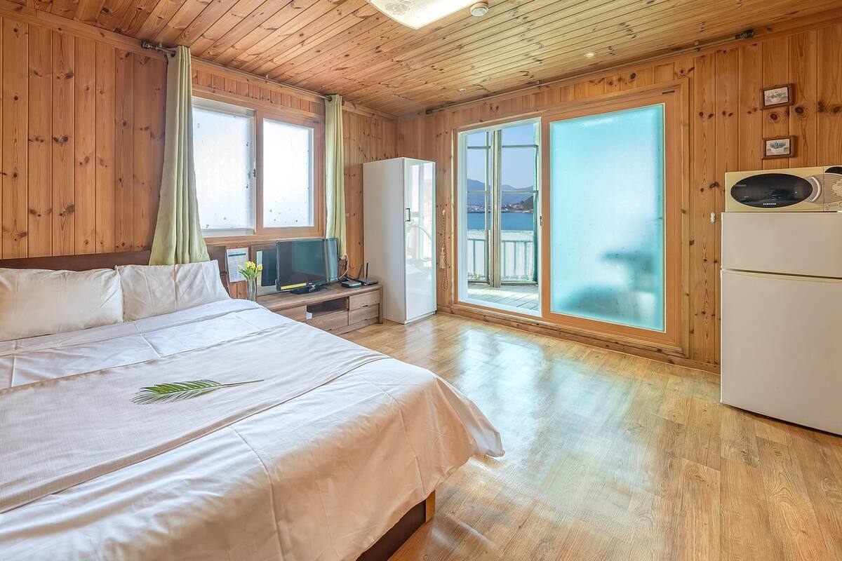 A wooden-paneled room with a bed, a television, a refrigerator, and a view of the outdoors.