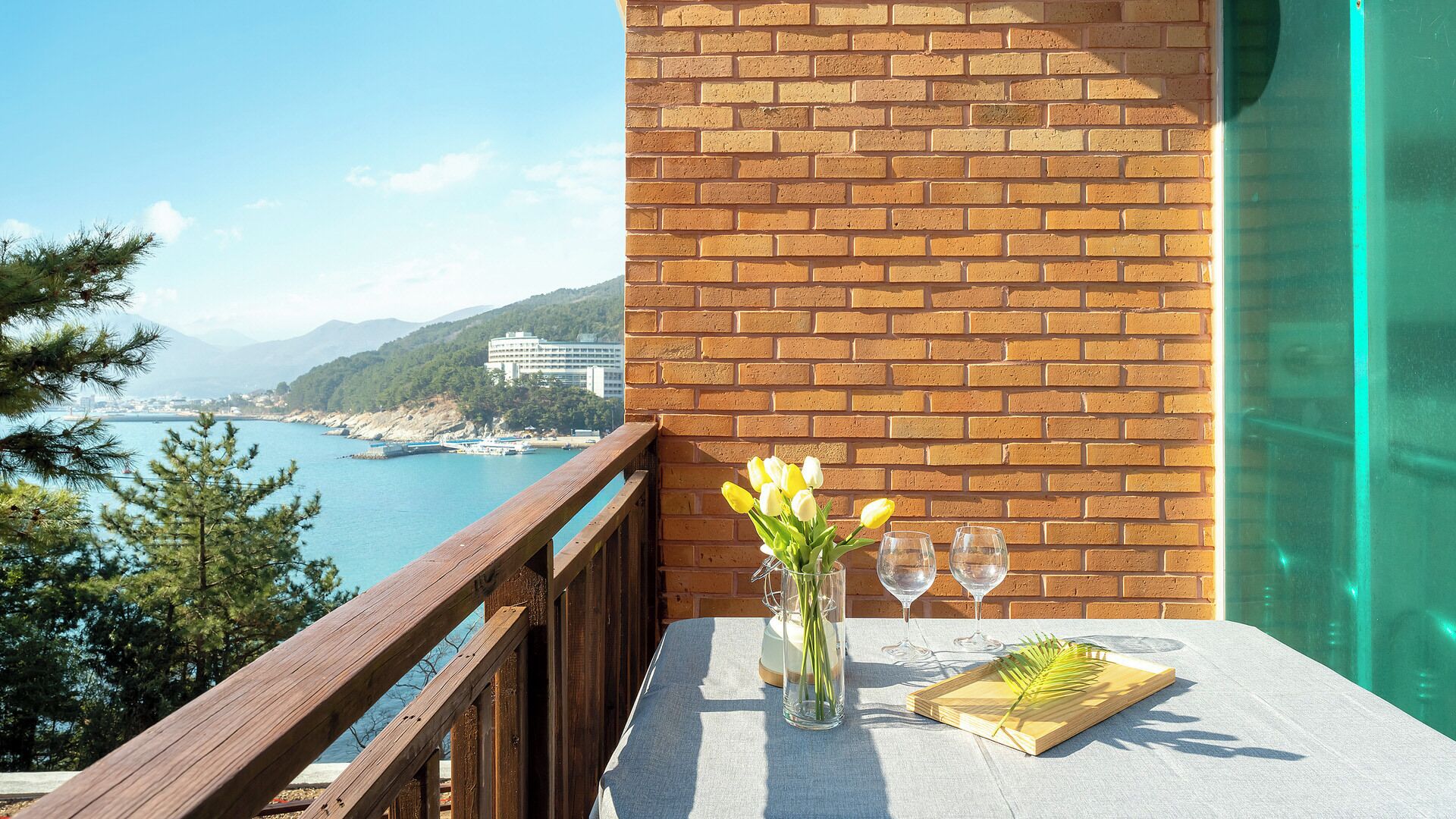A balcony with a wooden railing, a table with a vase of flowers, and two wine glasses.