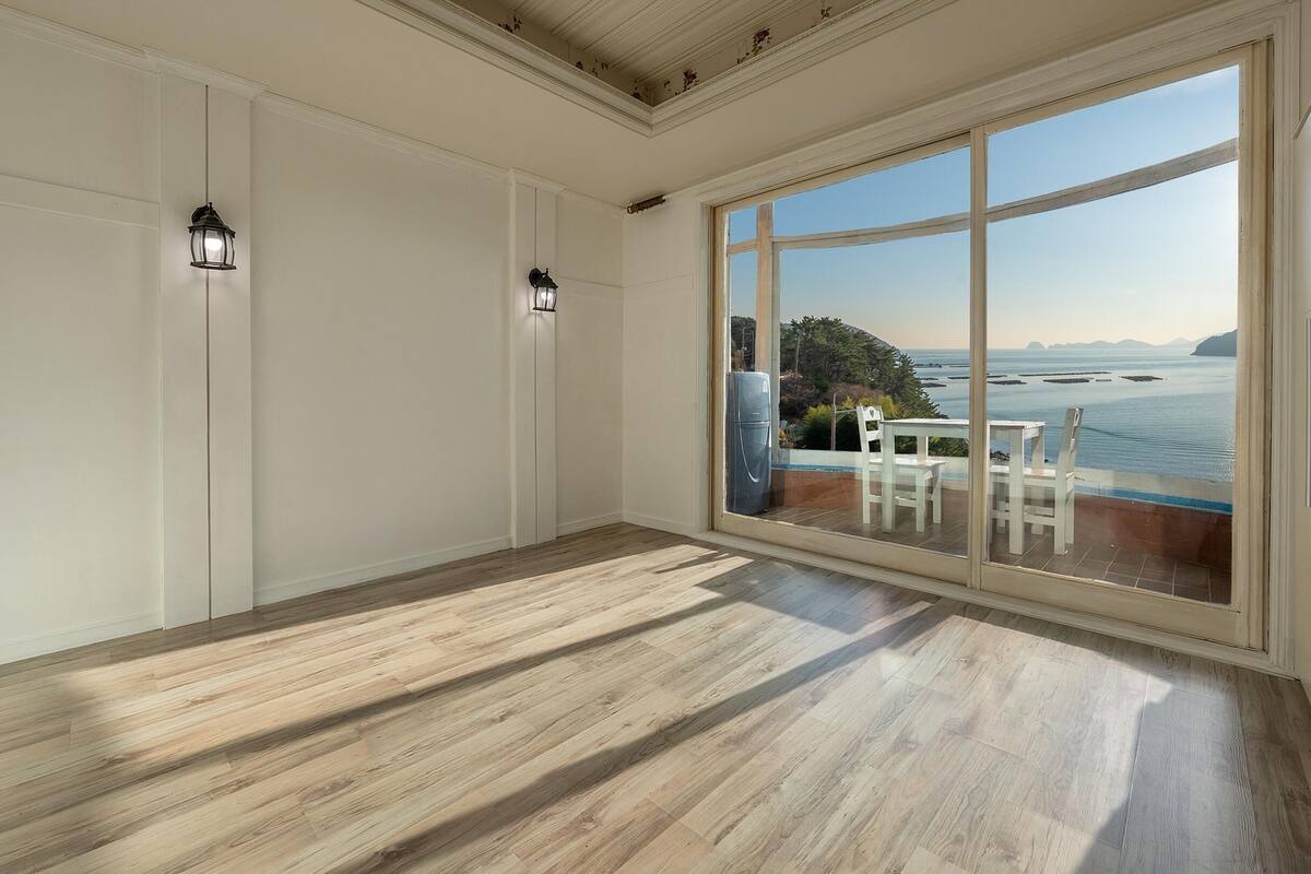 A spacious room with a large sliding glass door leading to a balcony with a view of the sea.