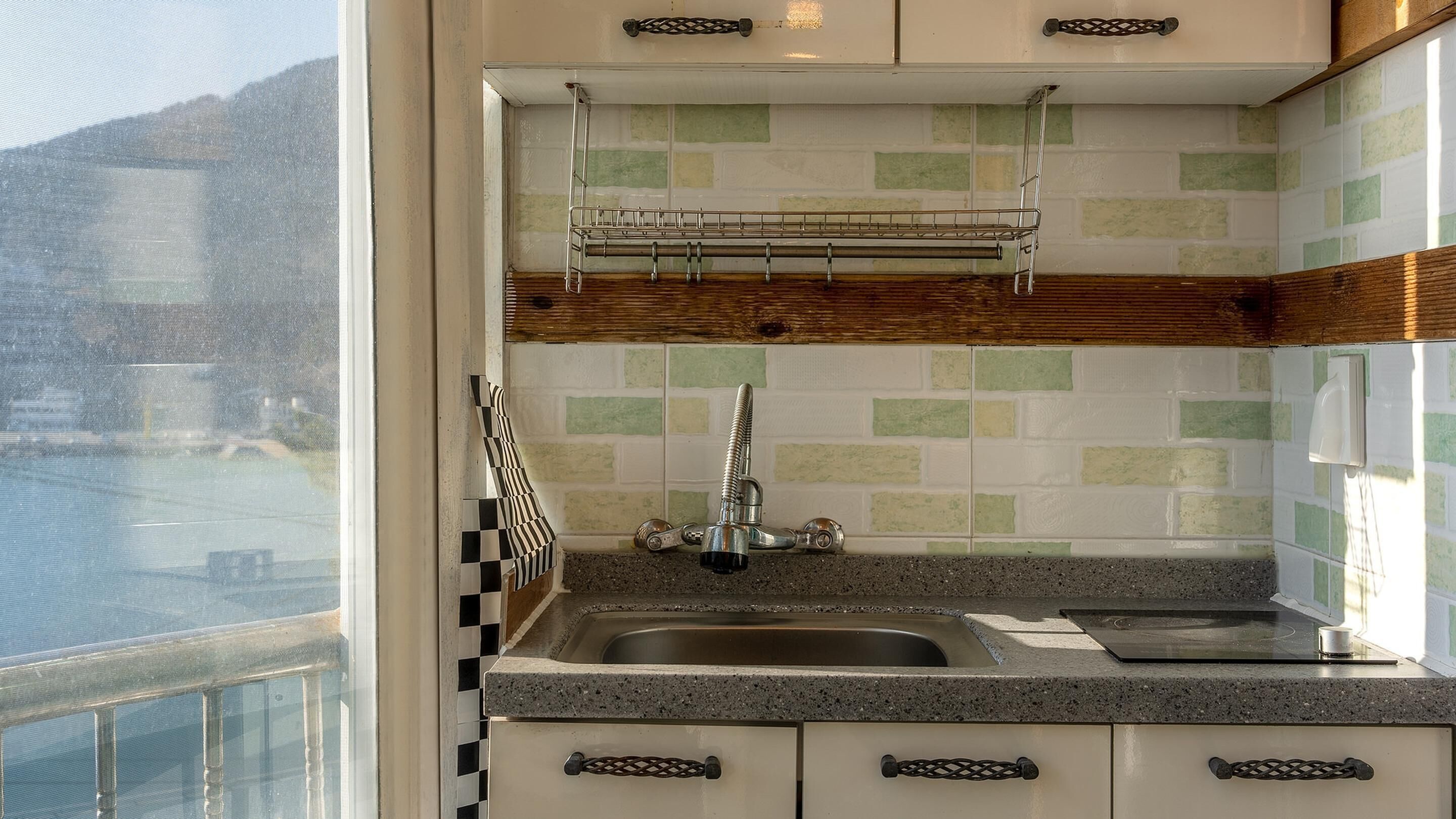 Una cocina con encimera de granito, pileta de acero inoxidable y ventana con vista al agua.