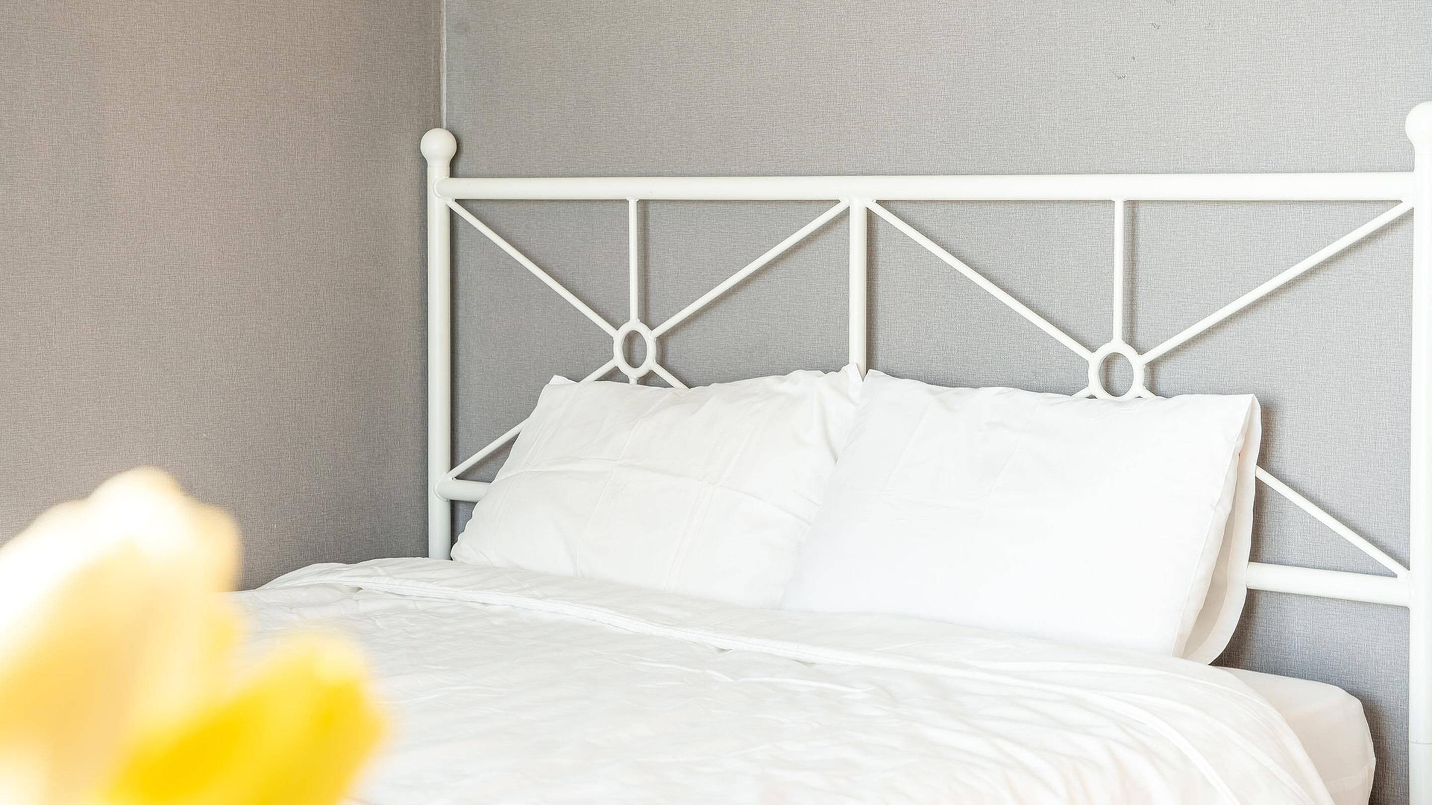 Una cama bien hecha con sábanas blancas y un cabecero de metal blanco en una habitación con paredes grises.