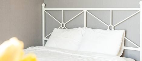 Una cama bien hecha con sábanas blancas y un cabecero de metal blanco en una habitación con paredes grises.