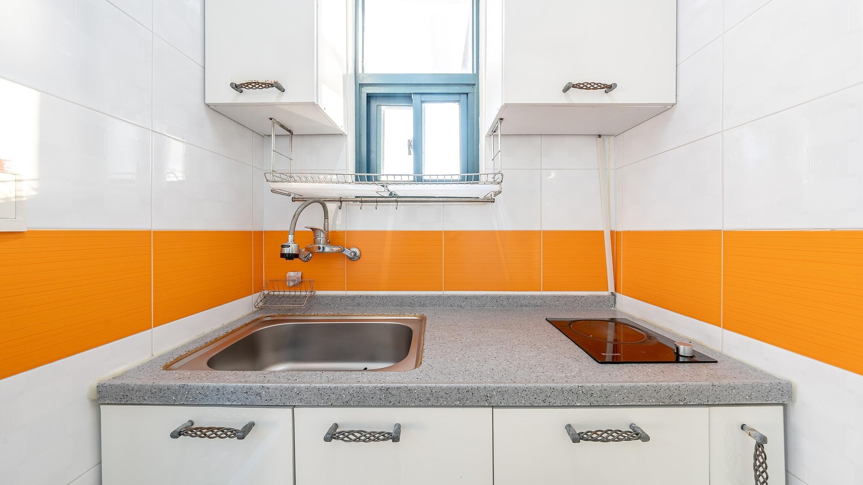 A kitchen with white and orange tiles, a window, a sink, and a stove.