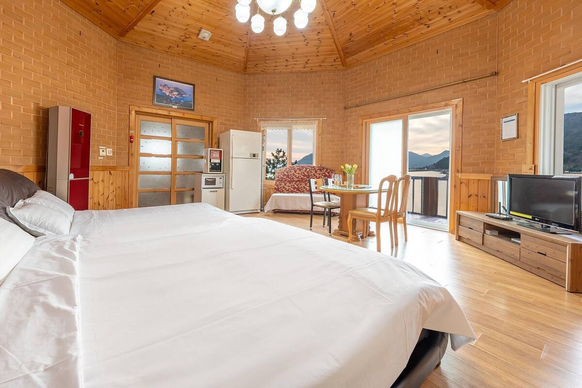 A bedroom with a large bed, a wooden ceiling, a TV, and a balcony with a view.
