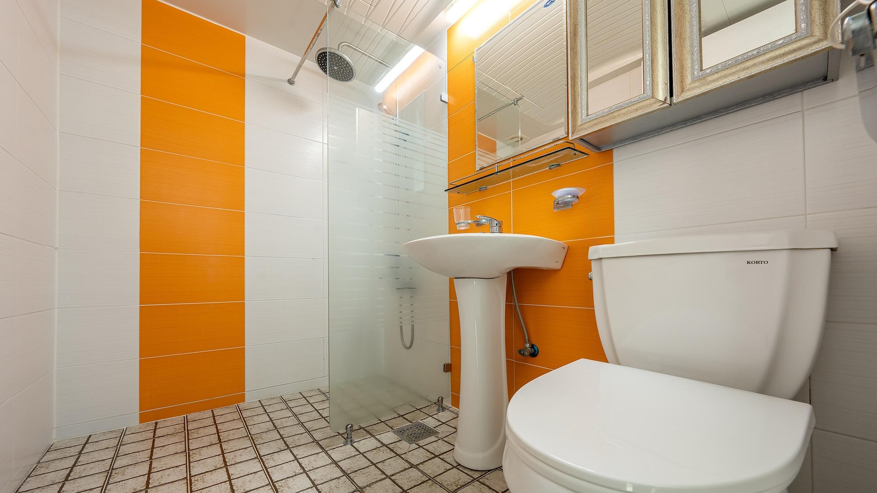 A bathroom with a white toilet, a sink, and a shower. The walls are tiled in orange and white.