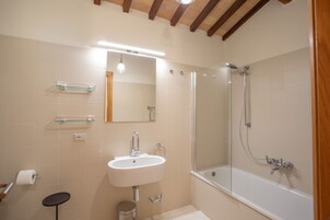 Un baño con un lavamanos blanco, estantes de vidrio, un espejo, una ducha y un techo de madera.