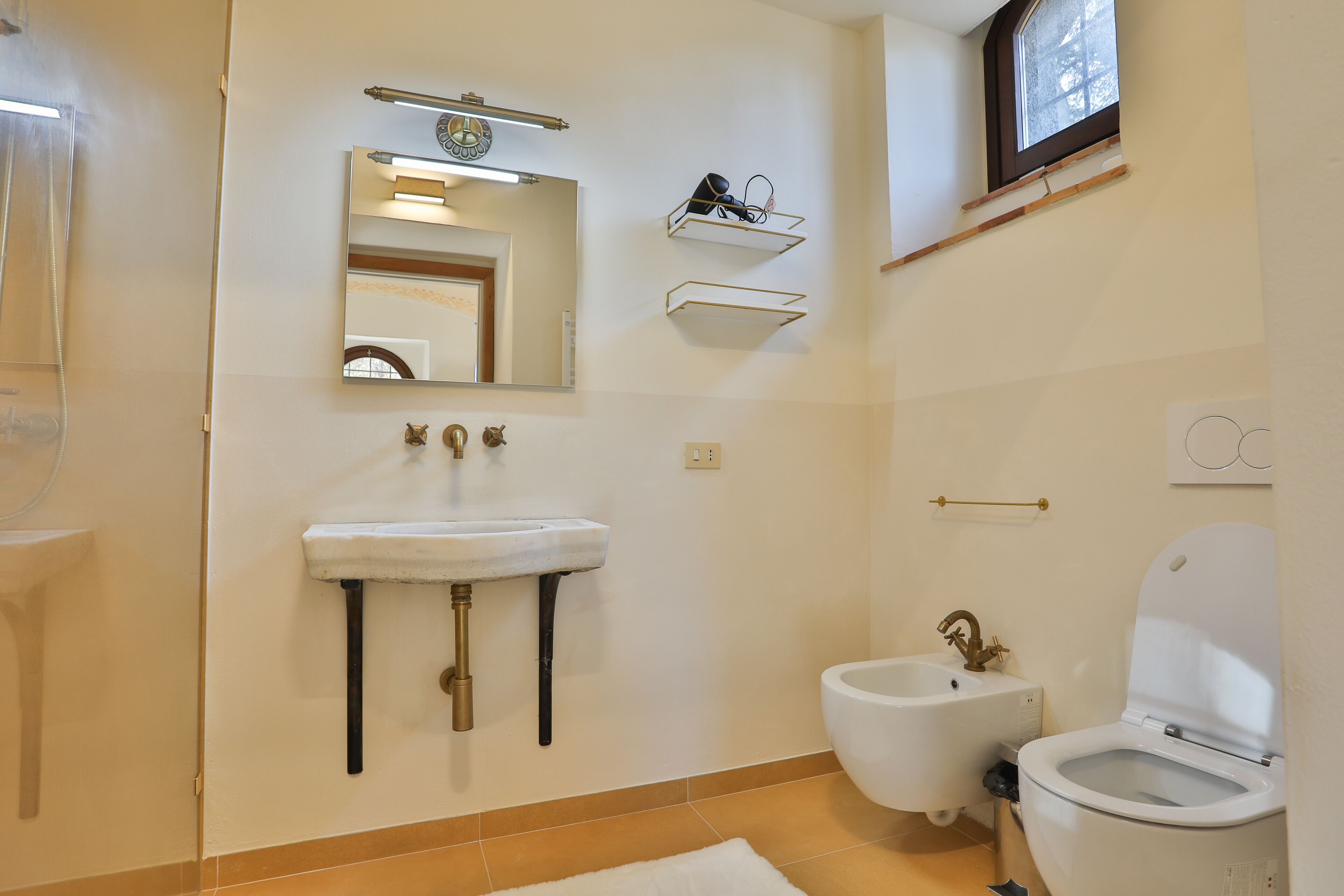 Un bagno con lavabo su piedistallo, bidet e water. Sopra il lavabo, due mensole a parete.