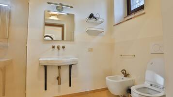 Un bagno con lavabo su piedistallo, bidet e water. Sopra il lavabo, due mensole a parete.