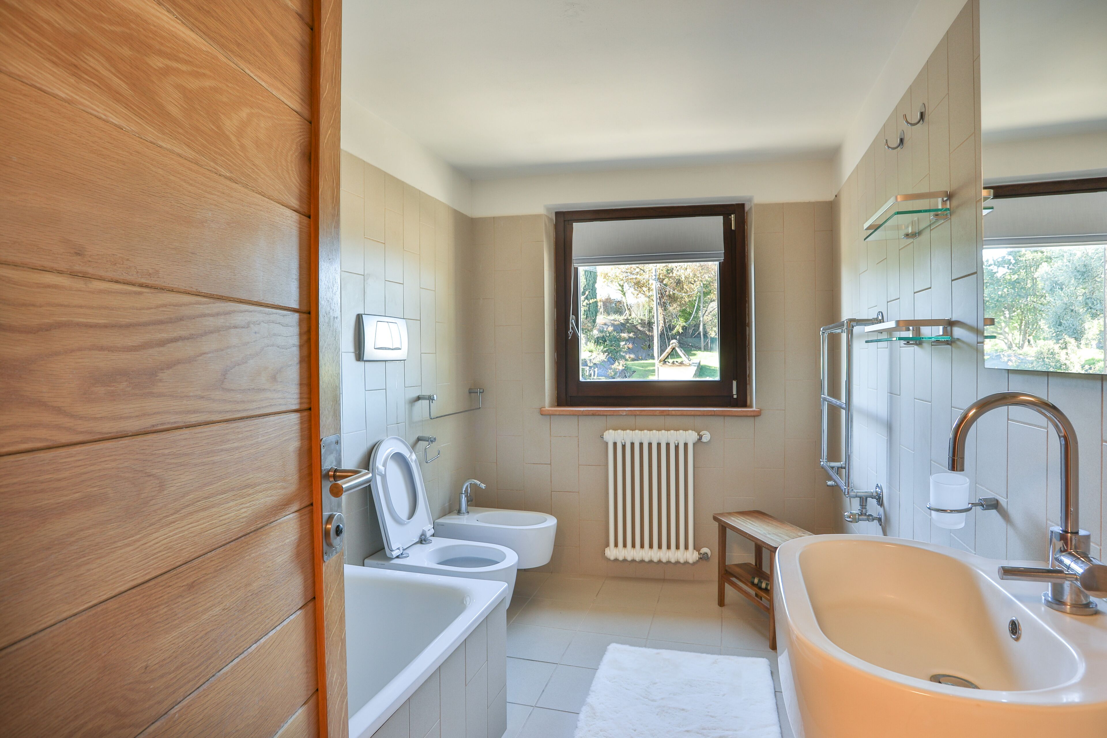 A modern bathroom with a bathtub, two sinks, a window, and a radiator.
