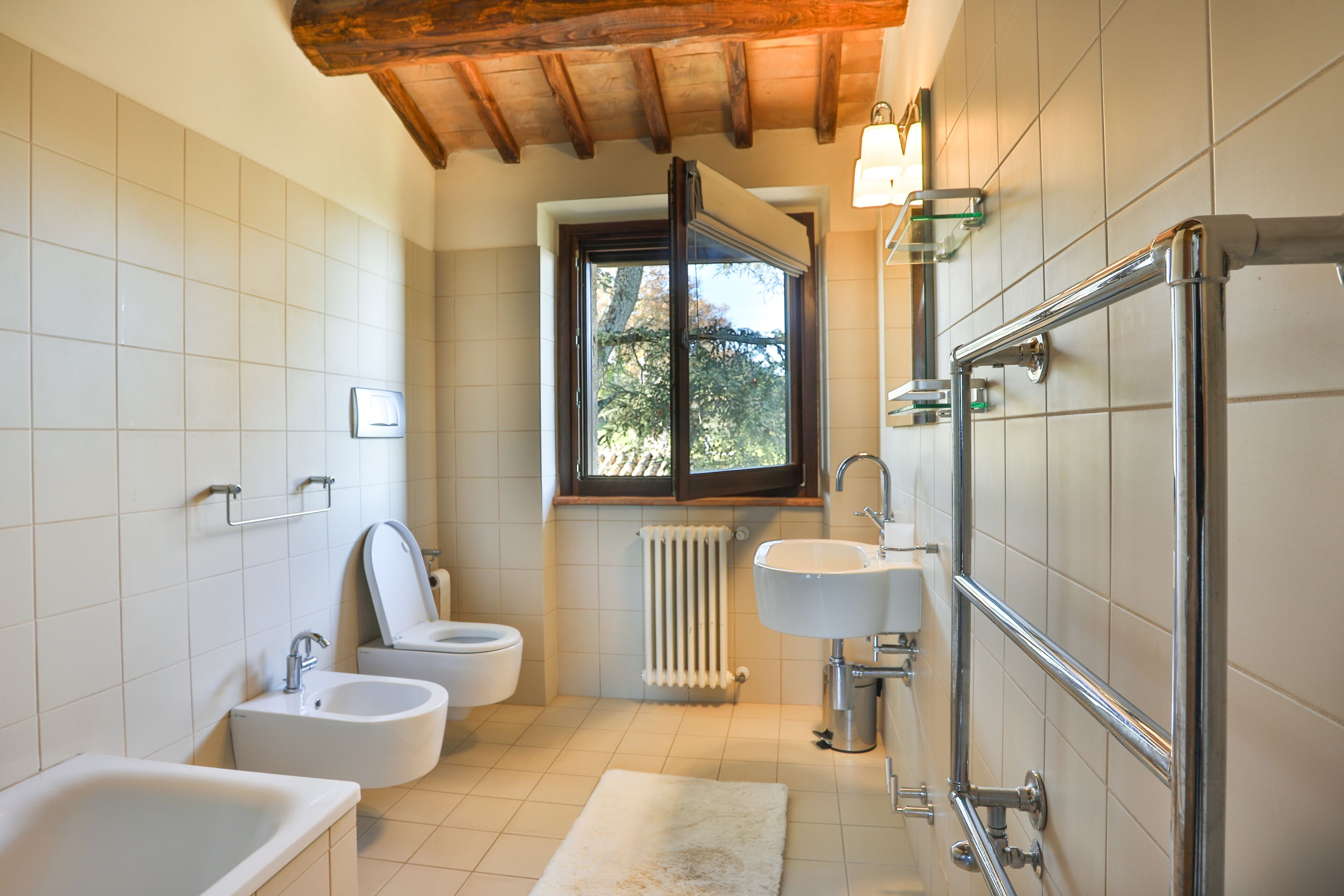 A bathroom with a bathtub, two sinks, a toilet, and a window with a view of trees.