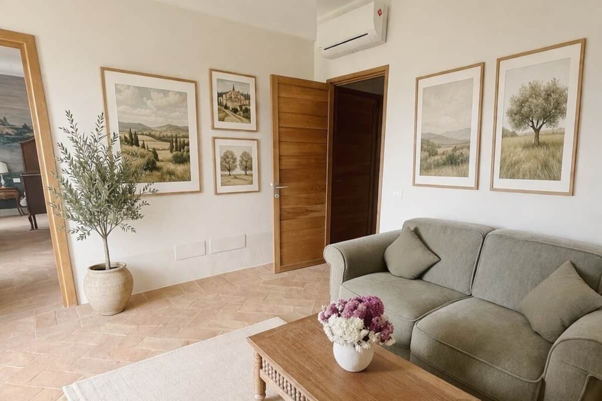 Una sala de estar con un sofá, una mesa de centro con un jarrón de flores, una planta en maceta y cuadros en la pared.