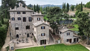 Un edificio de piedra con varias habitaciones, un patio con mesas al aire libre y un césped bien cuidado.