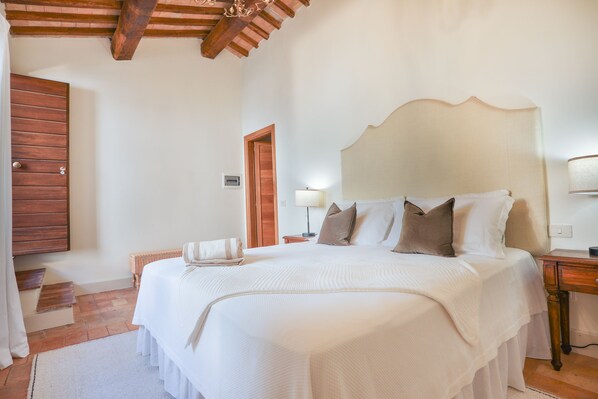 A bedroom with a large bed, a wooden headboard, a nightstand, a lamp, and a wooden door. - Pietra Campana (Orvieto)
