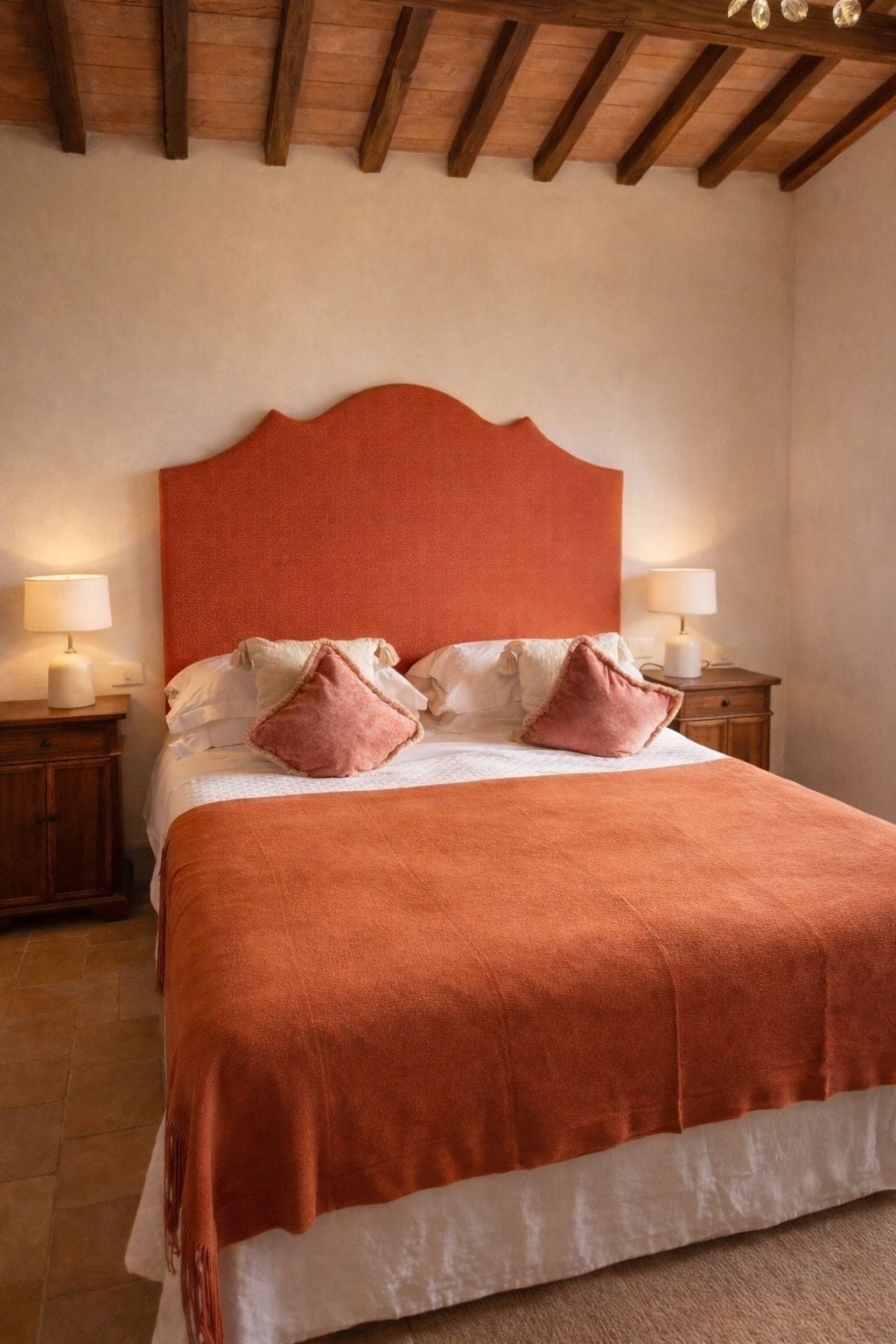 Un dormitorio con una cama grande, cabecera de madera, dos mesitas de noche con lámparas y techo de madera.